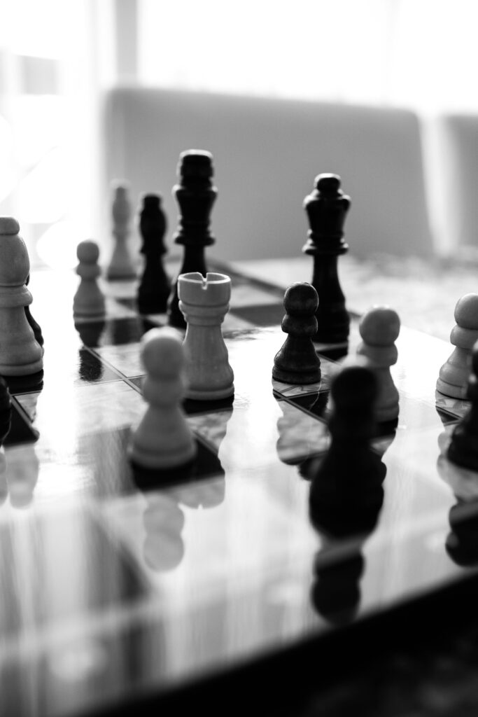 Monochrome chess pieces on a reflective board indoors, highlighting strategy and elegance.